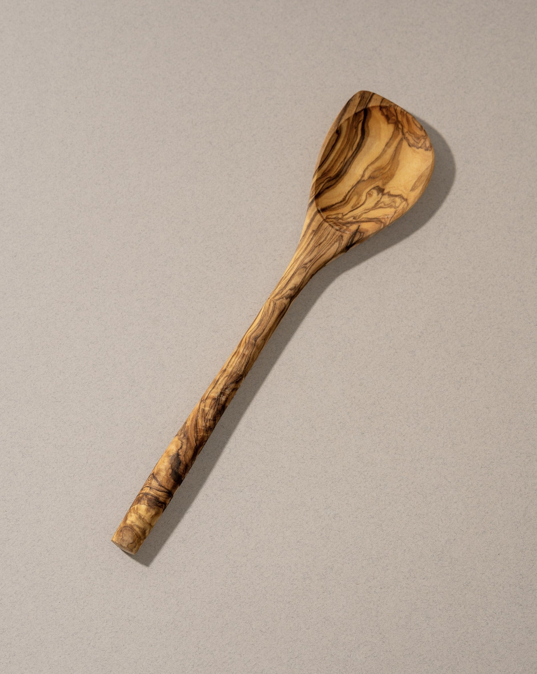 A natural olive wood pointed spoon with a unique grain pattern, handcrafted and displayed against a neutral background.