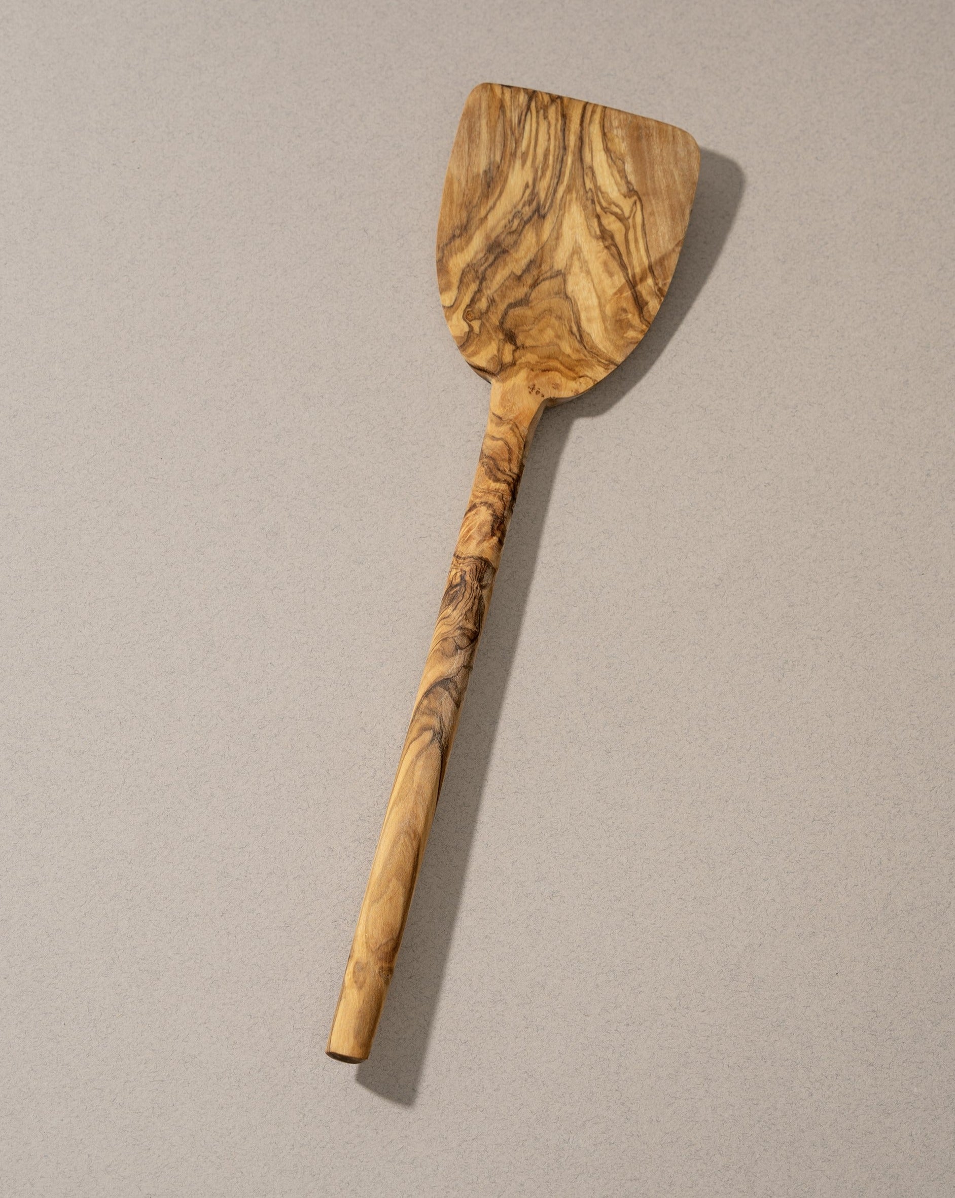 A wooden spatula with a natural olivewood pattern, lying on a grey surface.