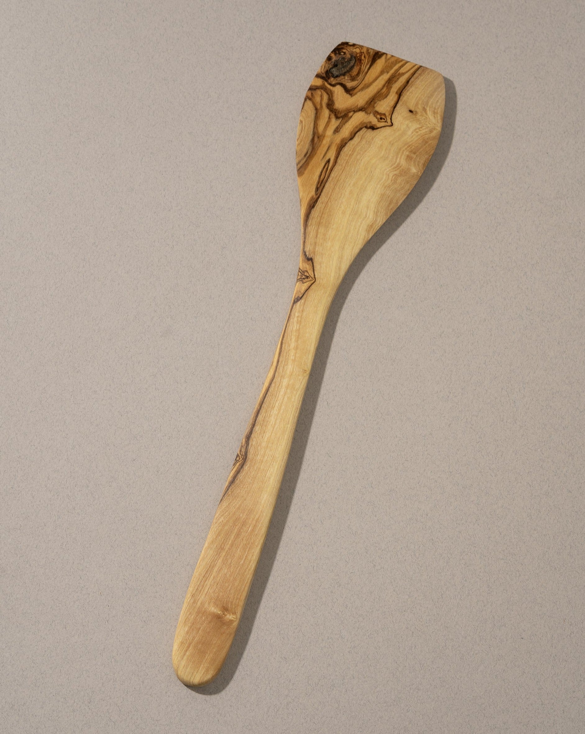 A large spatula made of natural olivewood with a smooth finish and characteristic wood grain patterns.