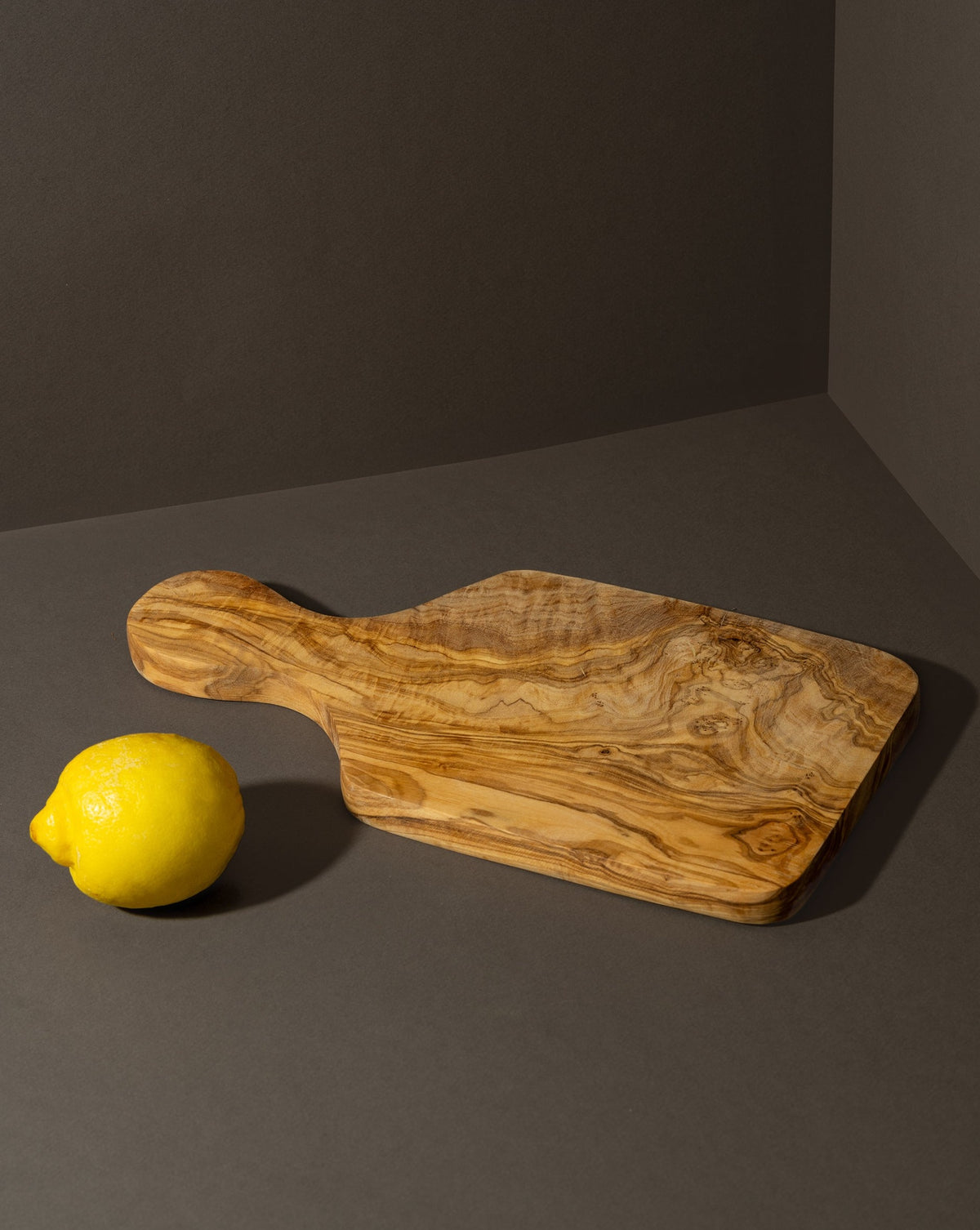 A rustic olive wood cheese board displayed with a lemon on a dark background.