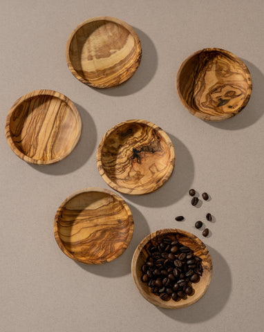 Natural olive wood ramekins displayed on a neutral background, with one ramekin filled with what appears to be coffee beans. The soft shadow enhances the rustic, handmade look of the pieces.