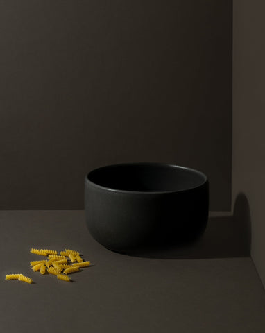 Matte black stoneware bowl with a few pieces of pasta placed beside it.