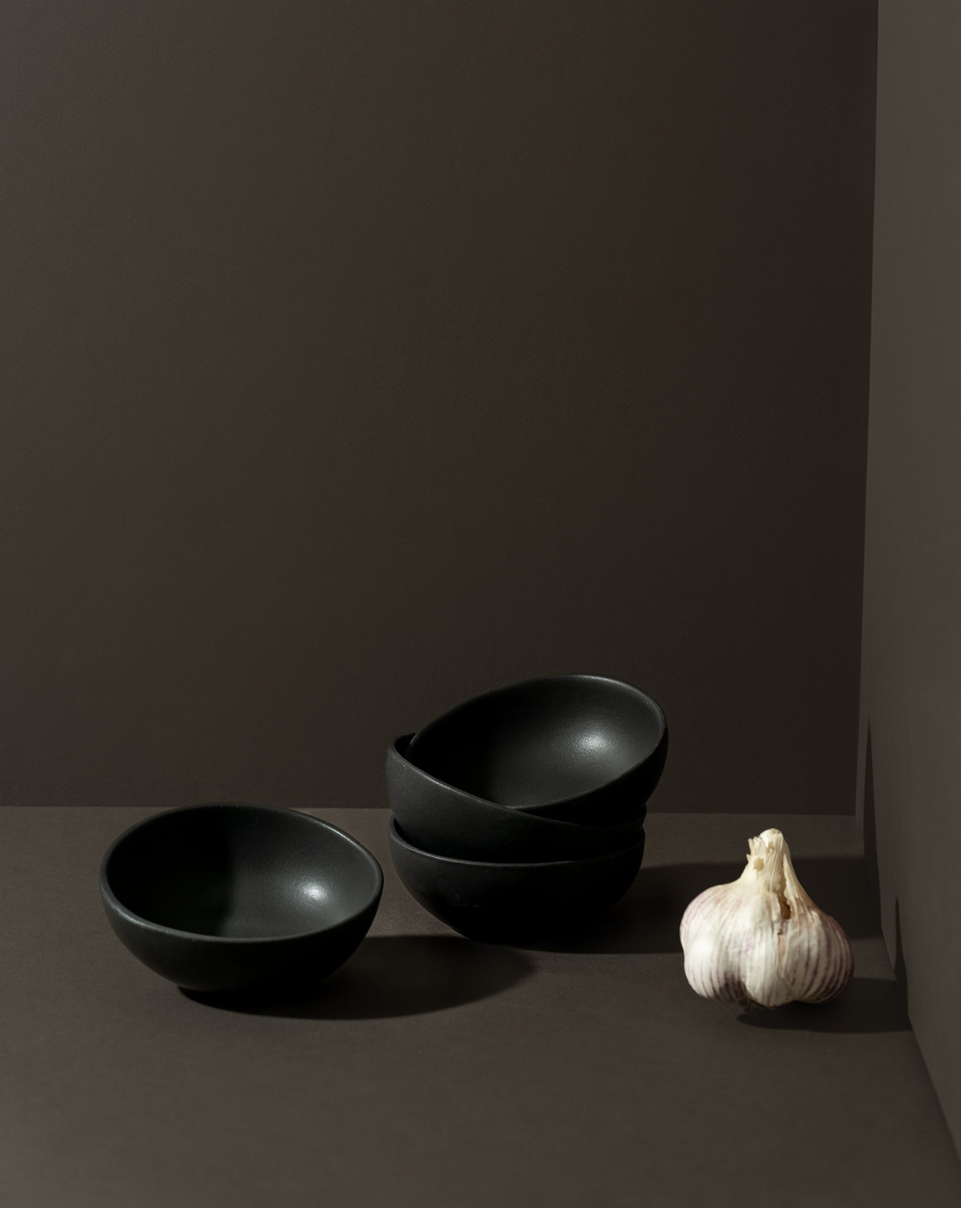 Three round stoneware condiment bowls in a matte finish, with one bowl containing some condiments, placed on a neutral background.