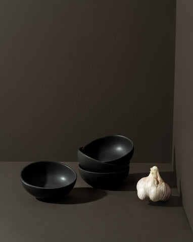 Three round stoneware condiment bowls in a matte finish, with one bowl containing some condiments, placed on a neutral background.