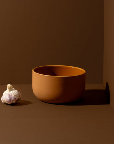 Terracotta-colored stoneware bowl with a whole onion placed beside it.