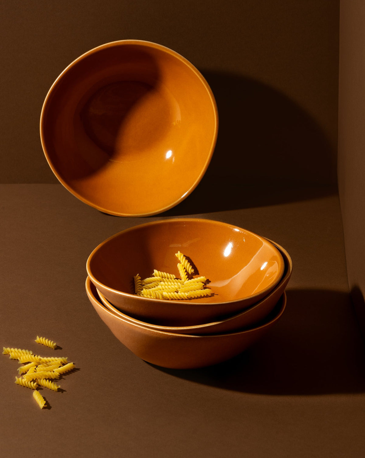 A beige stoneware soup plate with a matte finish, displayed alongside a white garlic bulb and a silver spoon, set against a neutral background with a textured napkin.