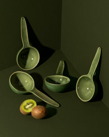 A stoneware bowl with a spoon shape, placed on a table with some food items, used as a serving dish for a meal.
