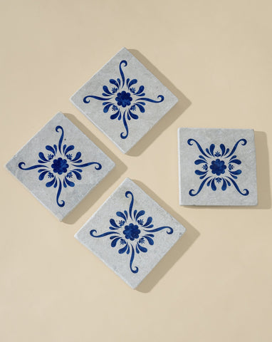 A set of four square white marble coasters with blue floral patterns, evenly arranged on a white background, showcasing their clean design and intricate detailing.