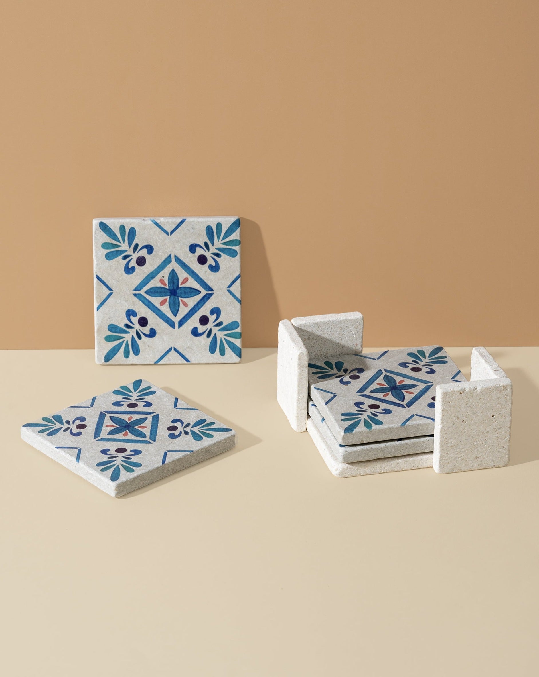 A set of square marble coasters with white and blue floral patterns, displayed alongside a holder.