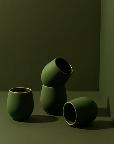 A set of four stoneware coffee cups arranged in a casual manner, with a matte green finish.
