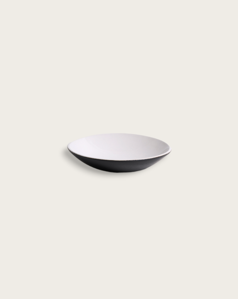 Two stoneware dessert plates with a matte finish, one containing some food residue, placed on a textured surface with a fork and spoon to the side.