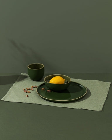 A green cotton placemat on a table with a plate and cup on top, against a dark background.