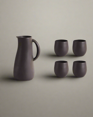 A stoneware jug in green color accompanied by four matching cups, displayed against a neutral background.