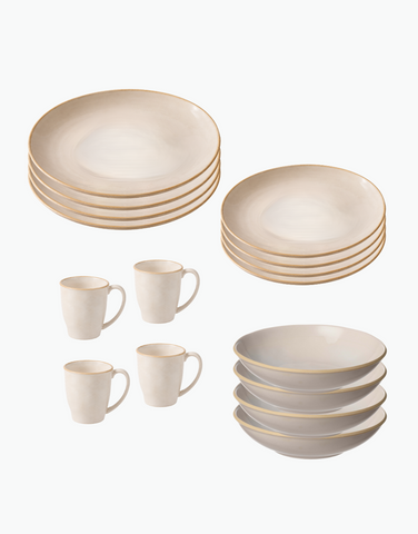 A ceramic dinnerware set in a warm cream or off-white glaze, featuring stacks of plates, bowls, and mugs with a subtle gold rim detail, arranged on a clean white background.