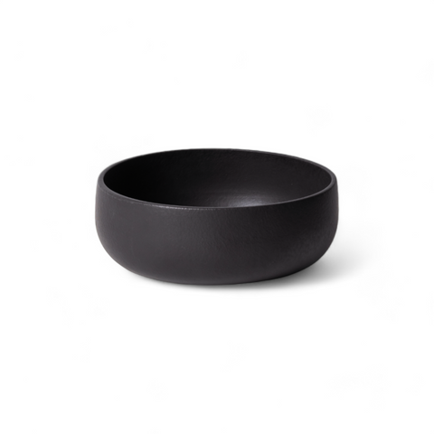 A plain matte black stoneware serving bowl displayed against a white background, highlighting its smooth finish and minimalist design.