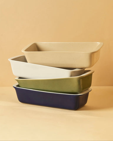 Four stoneware loaf pans stacked together in Glossy White/Cobalt Blue, Glossy White, Glossy White/Sage Green, and Speckled Cream. Each has a glossy finish and a clean, rectangular shape—perfect for baking bread or cake.