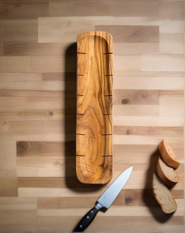 Olive wood bread slicing board laid flat with a knife beside it, and three pieces of bread placed nearby
