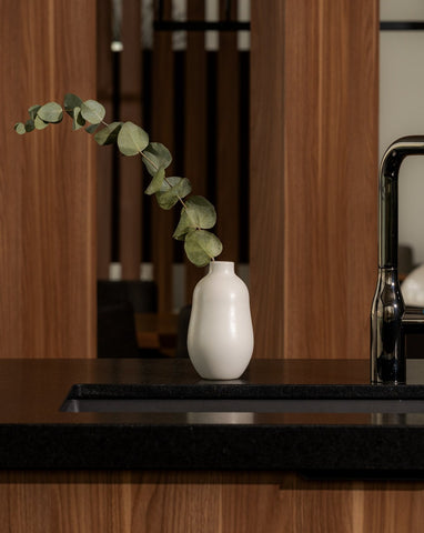 A white stoneware vase with a minimalistic design, placed on a surface and containing a green plant, showcasing its use as a decorative table accessory.