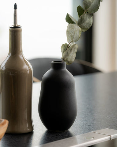 A white stoneware vase with a minimalistic design, placed on a surface and containing a green plant, showcasing its use as a decorative table accessory.