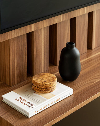 Matte black handmade stoneware vase with a minimalistic design, placed on a wooden table. Next to it is a set of four Natural Olive Wood Round Coasters stacked on top of a closed book.