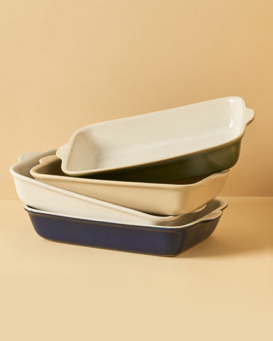 A stack of rectangular stoneware baking dishes in beige, blue, and green colors.