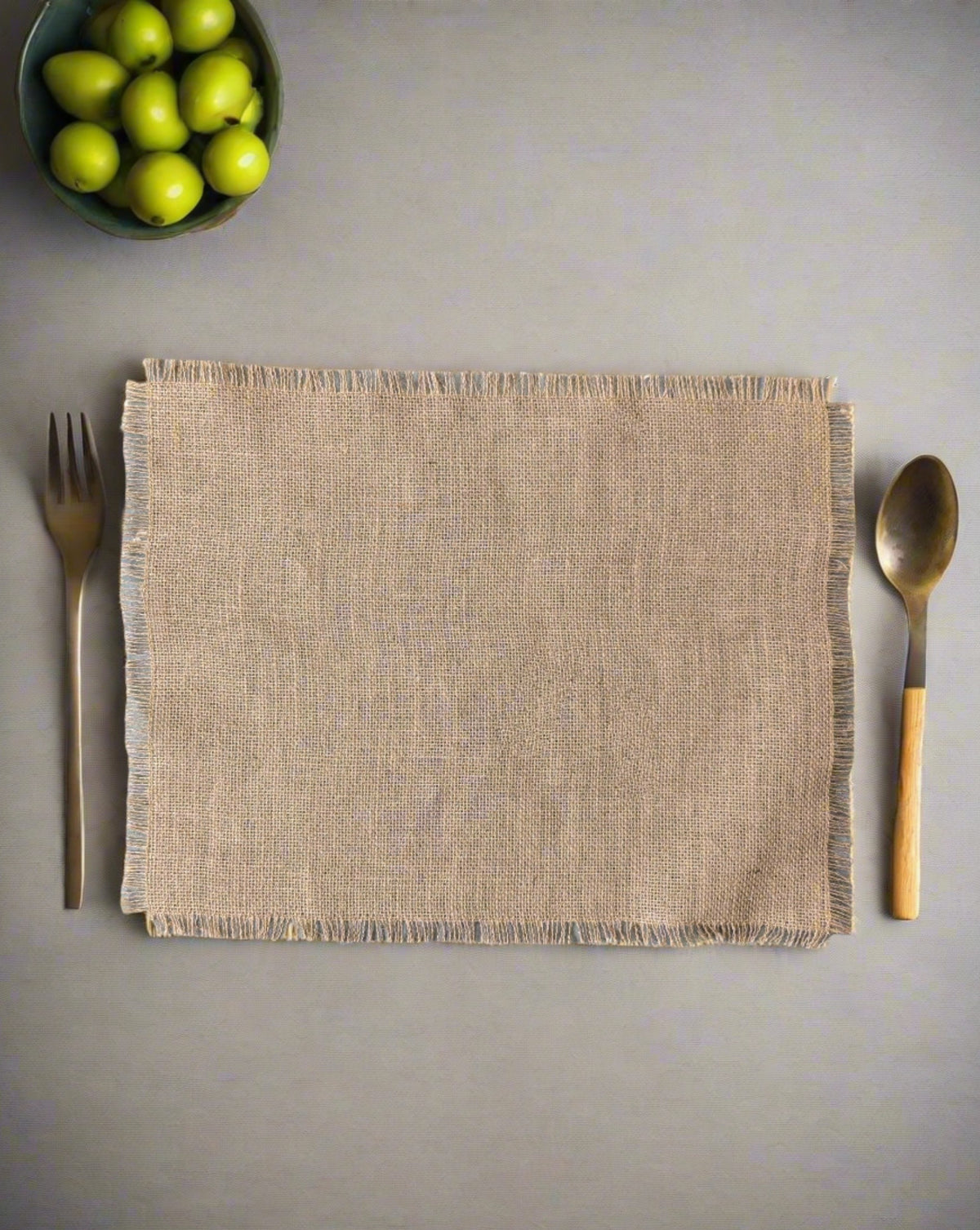 A beige burlap placemat on a gray surface with a fork on the left side and a spoon on the right side, both with wooden handles.