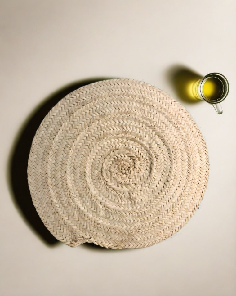 A beige palm fiber placemat on a white surface with a small glass dish and a spoon on top of it.