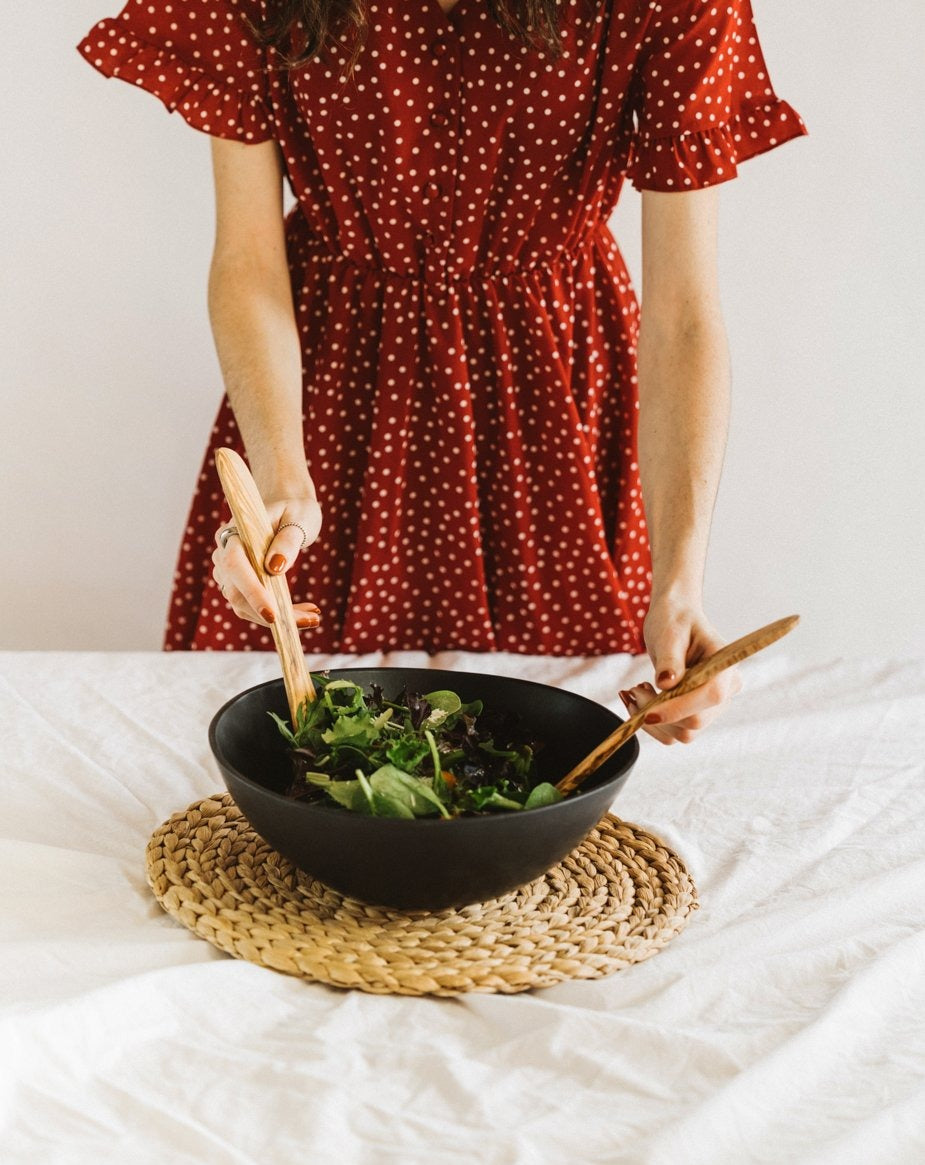 White stoneware serving bowl filled with salad, with a natural olive wood spatula used for mixing.