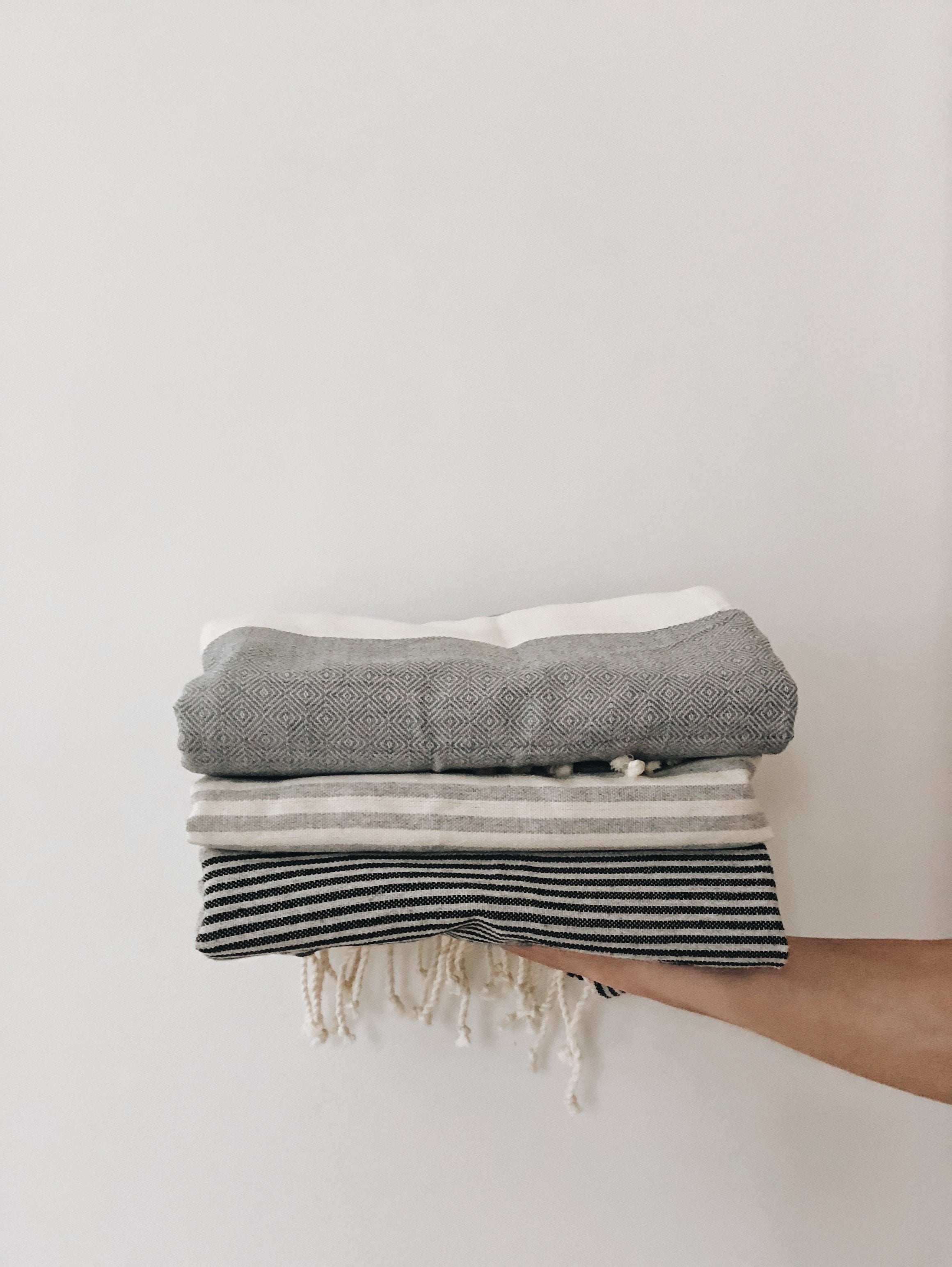 A gray fouta towel with black stripes, neatly folded and held up by hand to showcase its texture, pattern, and lightweight fabric.


