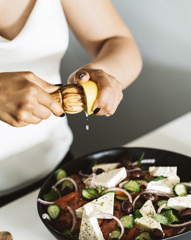 Person using a wooden lemon press to squeeze lemon juice over a bowl of salad on the table