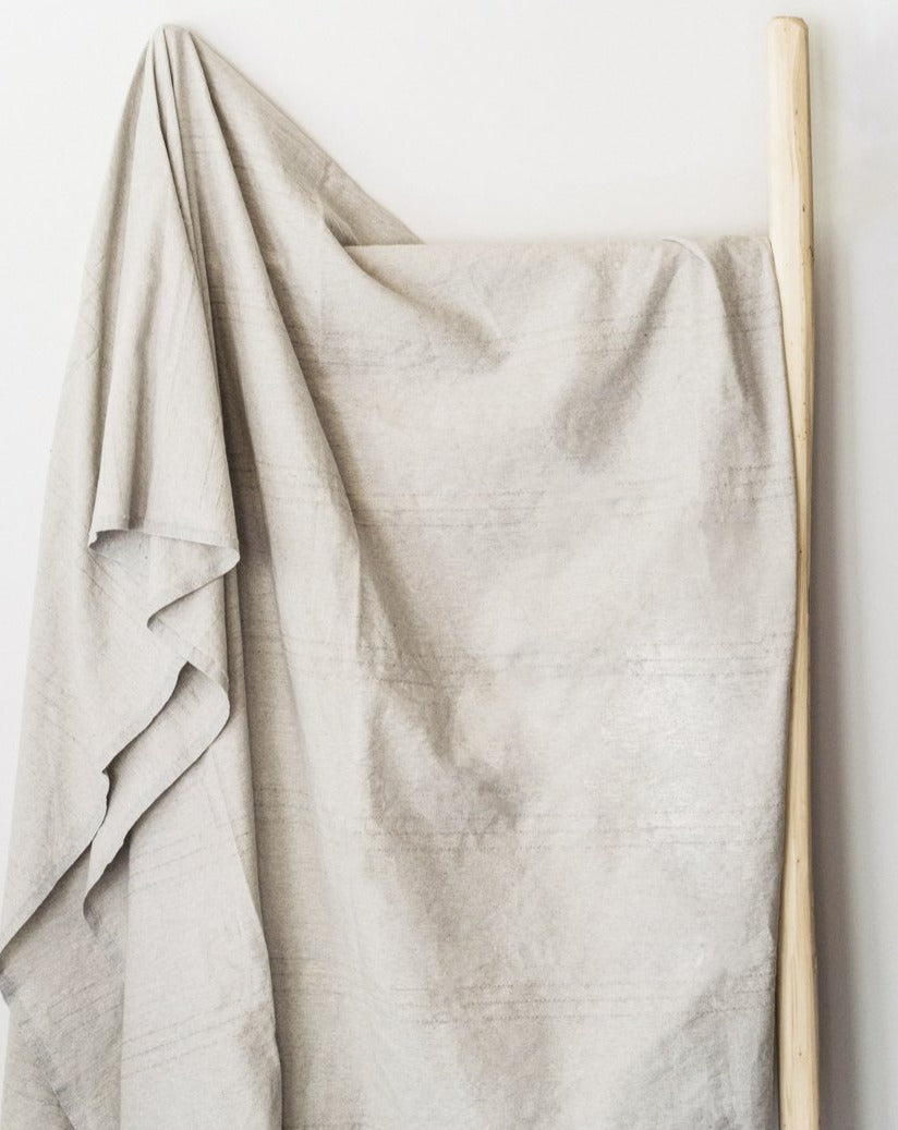 A gray fouta towel hanging vertically against a white background, showcasing its simple design and decorative tassels.

