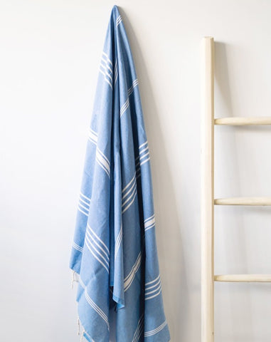 A blue fouta towel with white stripes hanging on a wall next to a wooden ladder.
