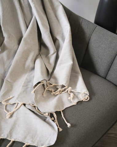 A gray fouta towel draped over the back of a sofa, with decorative tassels hanging down.